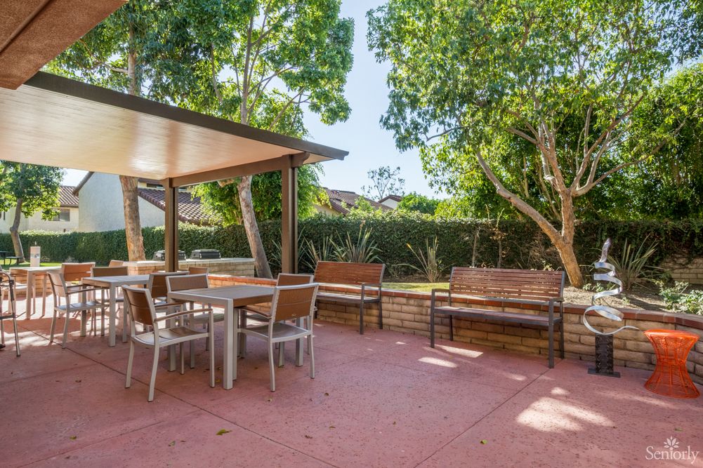 A spacious outdoor patio with tables, chairs, and a shaded seating area surrounded by lush trees.