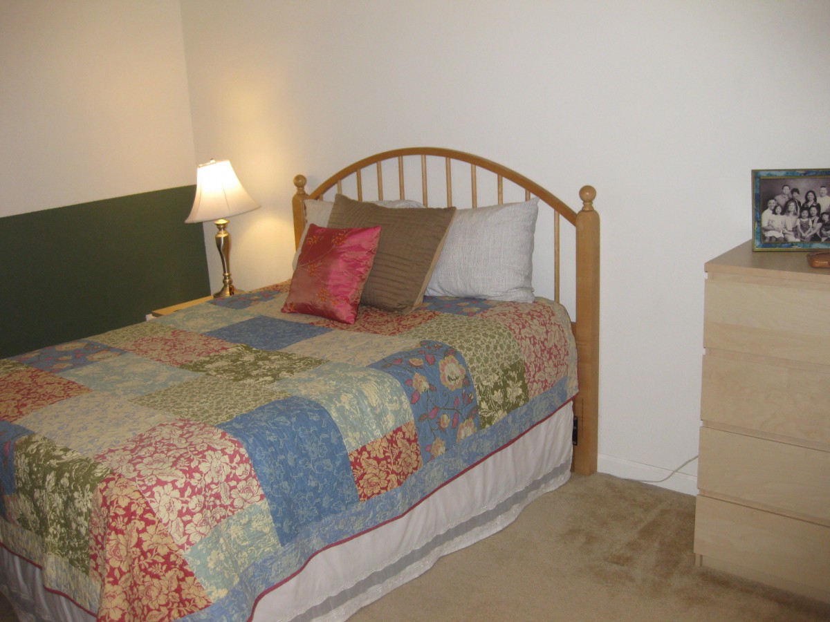 A cozy bedroom with a wooden bed frame, colorful quilt, and bedside lamp.