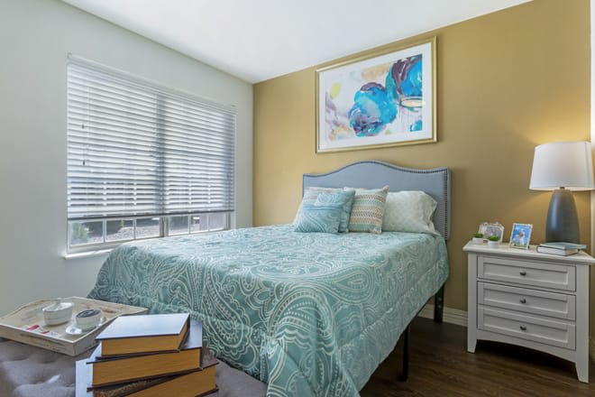 A cozy bedroom with a neatly made bed, showcasing soft natural light from the window and a piece of abstract artwork on the wall.