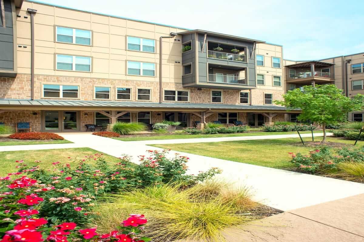 A modern residential apartment building with well-maintained gardens in front.