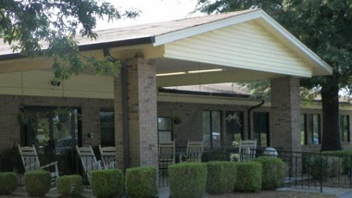 A cozy outdoor seating area under a roof, surrounded by neatly trimmed bushes.