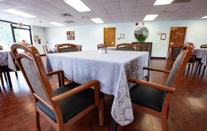 A neatly set dining room table with a white tablecloth and wooden chairs in a spacious interior.