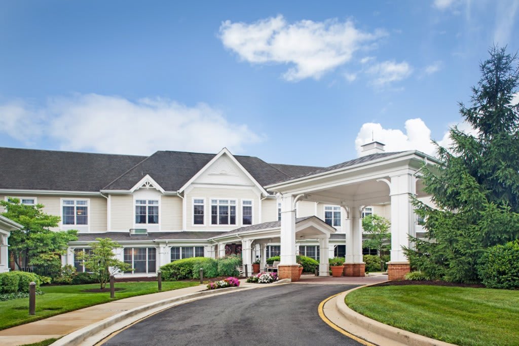 A large residential building with a circular driveway and manicured landscaping under a blue sky with clouds.