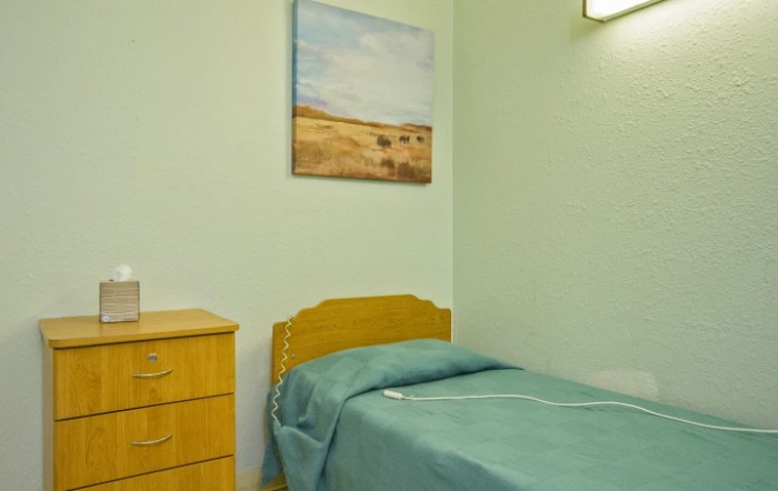 A minimalist bedroom with a single bed, a wooden dresser, and a landscape painting on the wall.