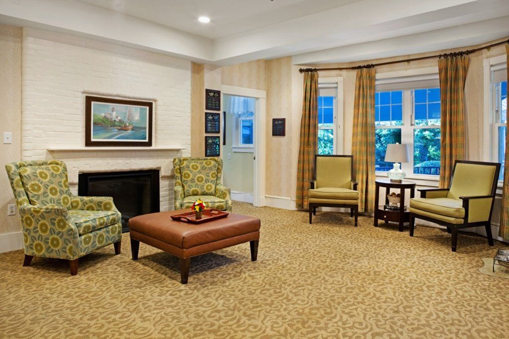 A cozy living room featuring comfortable chairs, a wooden coffee table, and a fireplace, adorned with elegant curtains and a painting on the wall.