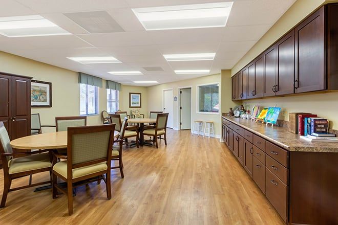 A spacious and well-lit dining area featuring wooden floors, tables, chairs, and cabinetry.