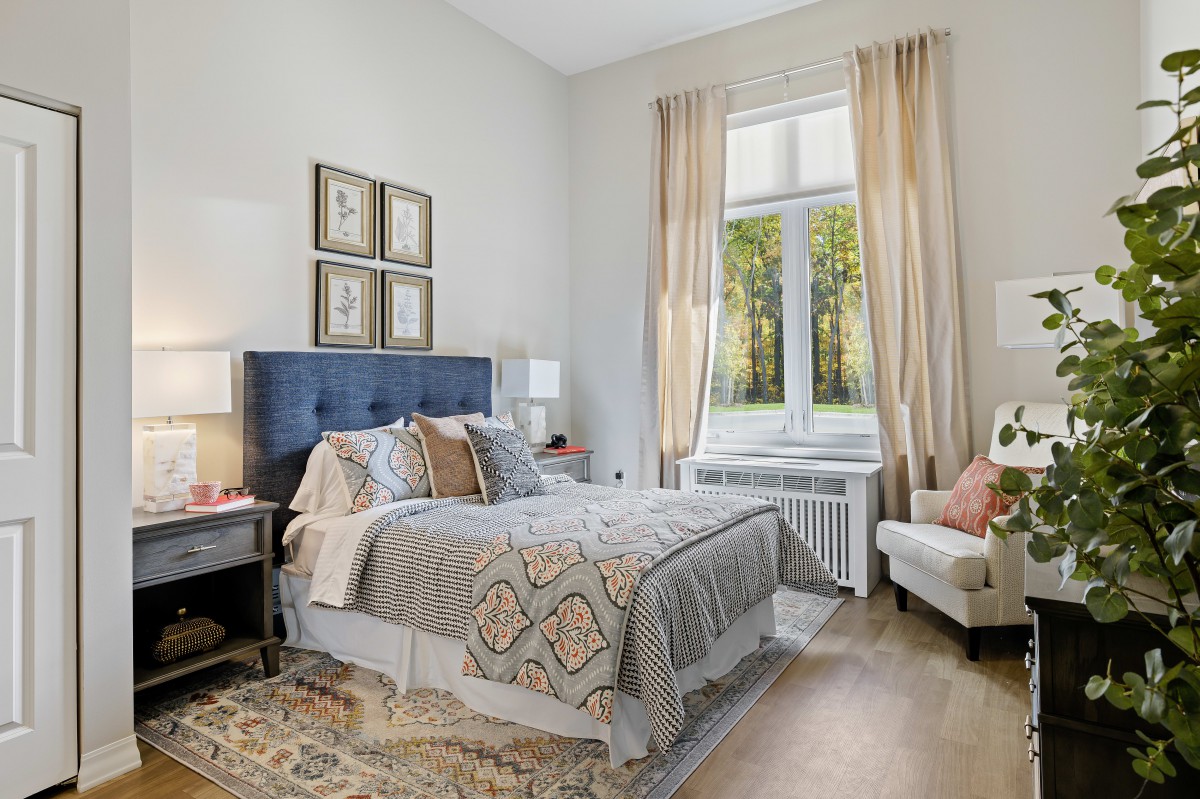 A well-decorated bedroom with a plush bed, elegant decor, and a large window with curtains.