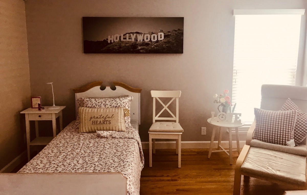 A cozy bedroom featuring Hollywood-themed artwork above a neatly made bed and chairs.