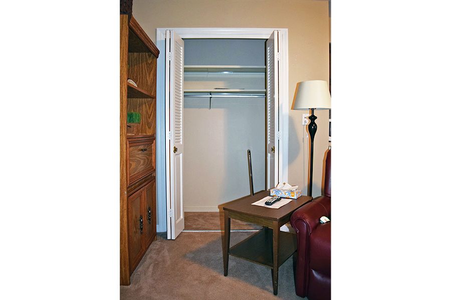 An open closet in a room with a small table, lamp, and chair nearby.