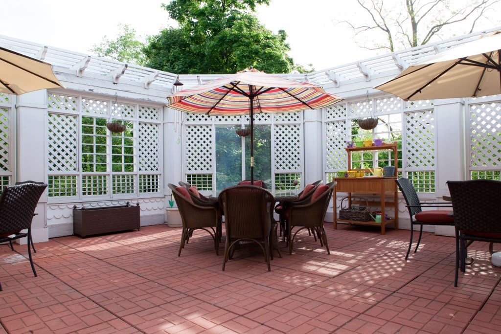 A sunny patio with outdoor furniture, including a table and chairs under umbrellas.