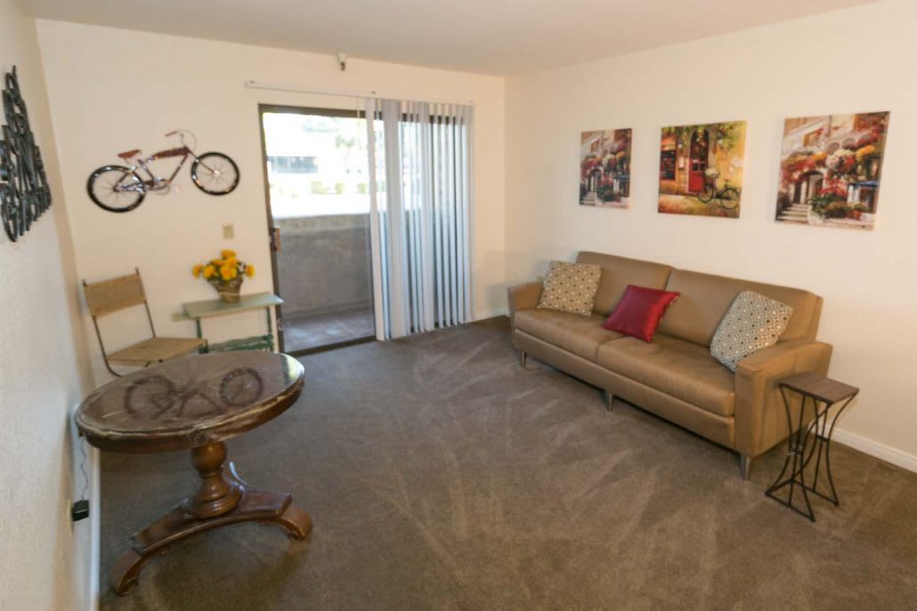 A cozy living room featuring a comfortable sofa, a small coffee table, and wall artwork, with a balcony visible through the sliding glass door.