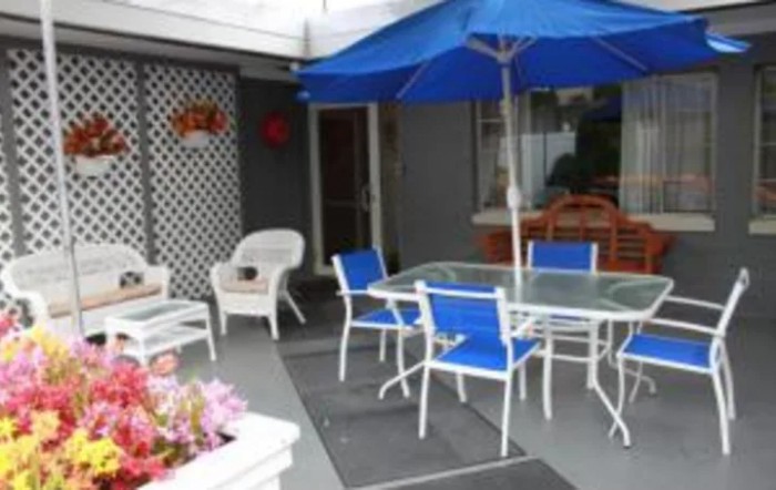 A cozy patio setup with a glass-top table, blue chairs, and an umbrella.