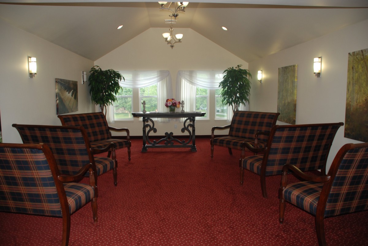 An elegantly furnished chapel room with red carpet, decorative seating, and natural light.