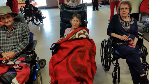 An elderly individual resting in a wheelchair, wrapped in a cozy blanket at a care facility.
