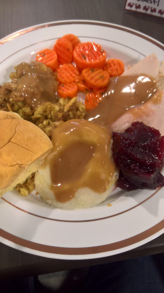 A classic Thanksgiving dinner plate with turkey, gravy, cranberry sauce, stuffing, mashed potatoes, carrots, and a bread roll.