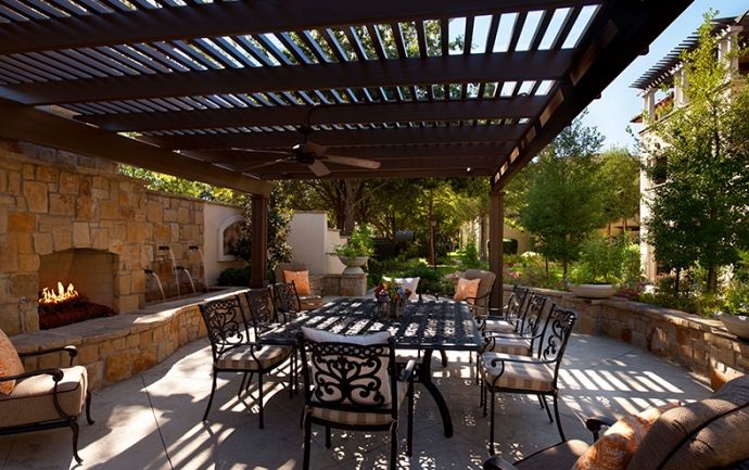 A cozy outdoor patio with a pergola providing shade over table and chairs, surrounded by lush garden greenery.