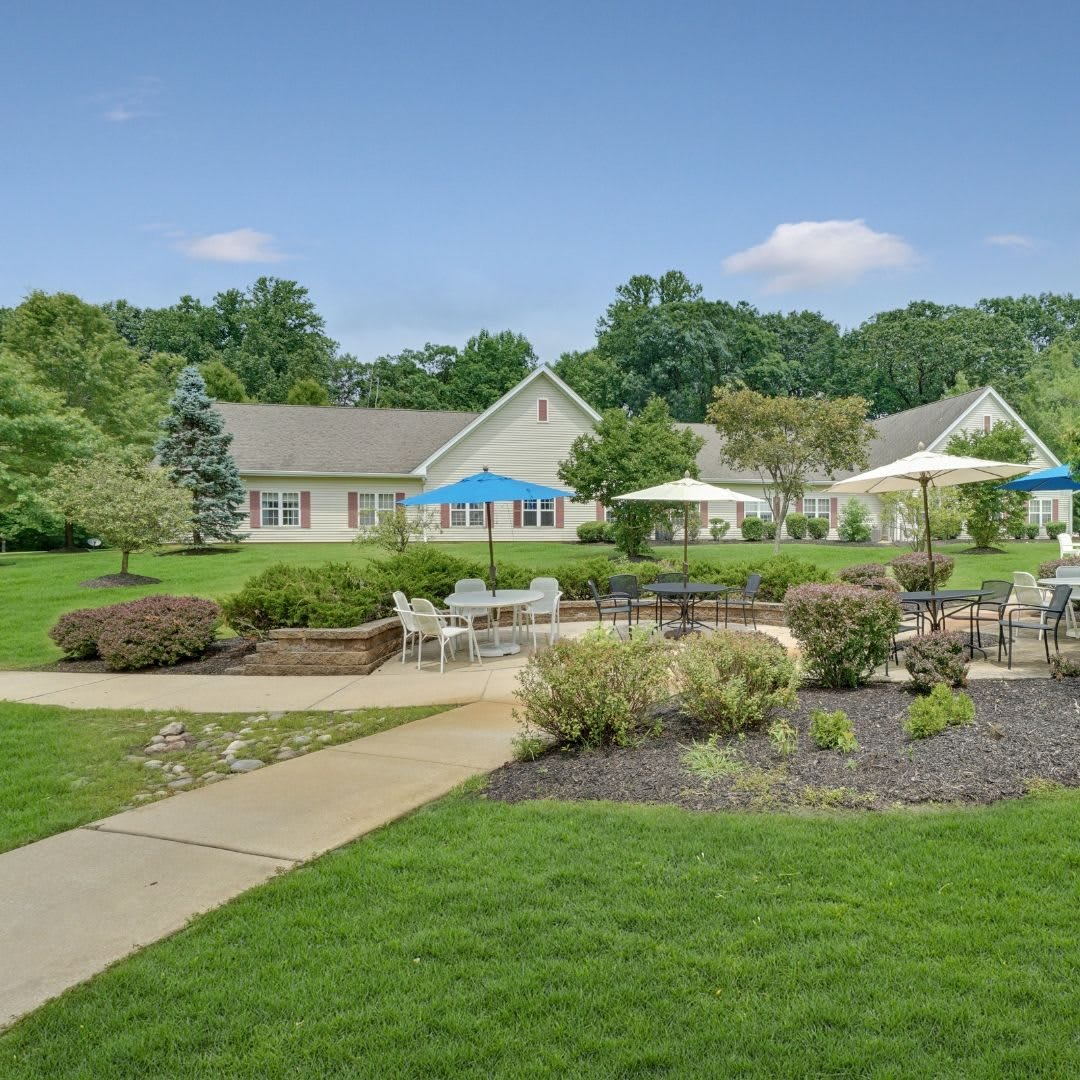 A scenic view of a well-maintained garden with outdoor seating, surrounded by lush greenery and a pathway leading to the building.