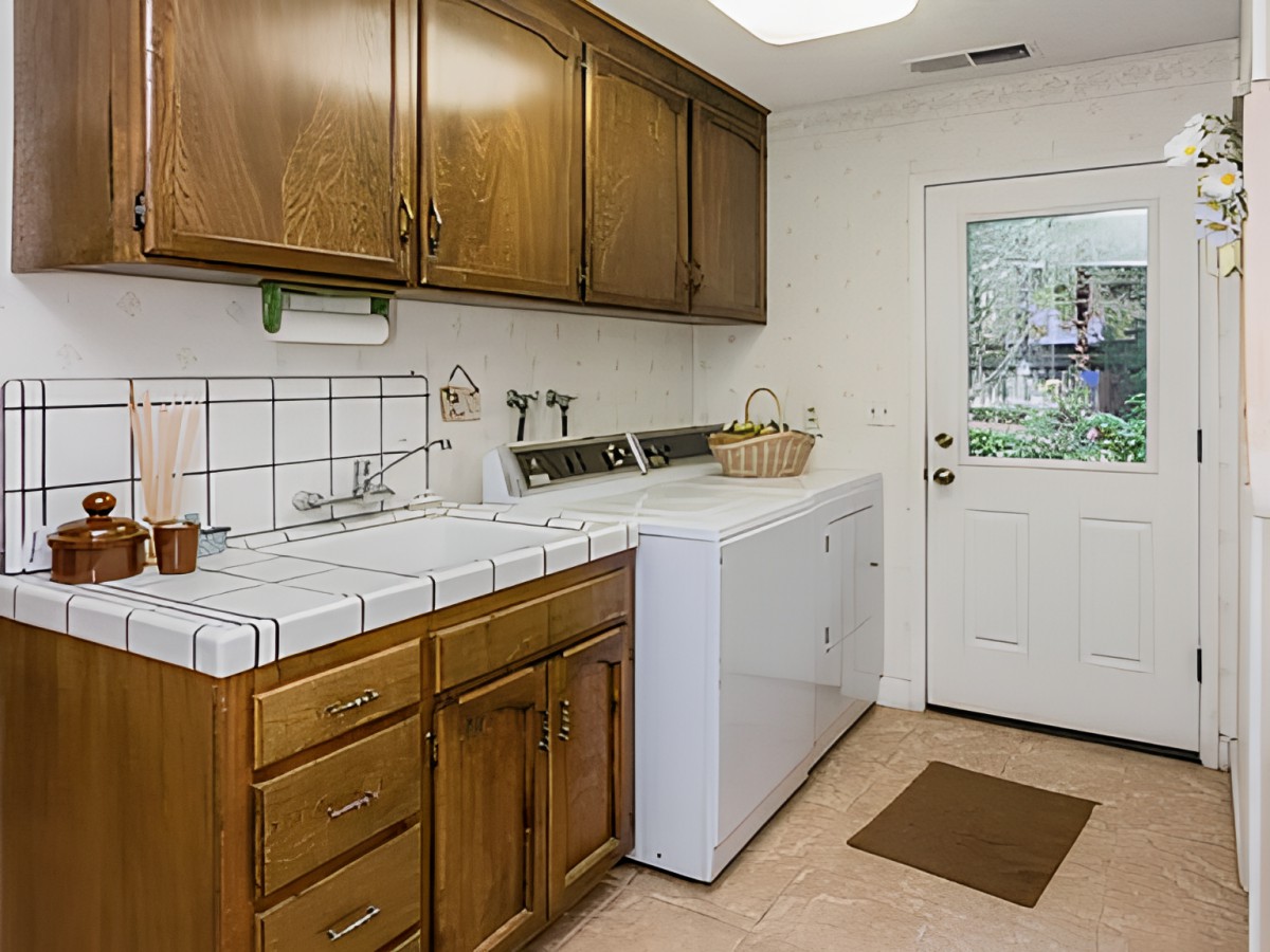 A well-organized laundry room with wooden cabinets, a washing machine, and a tile countertop.