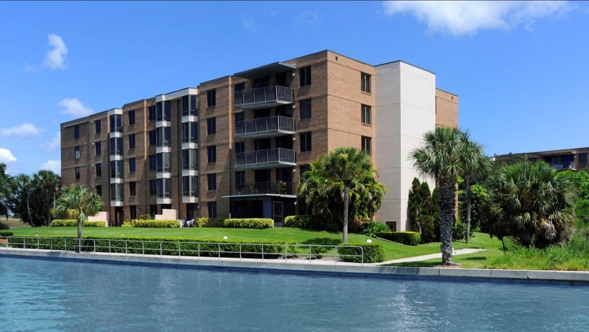 A waterfront apartment building with palm trees and a clear blue sky.
