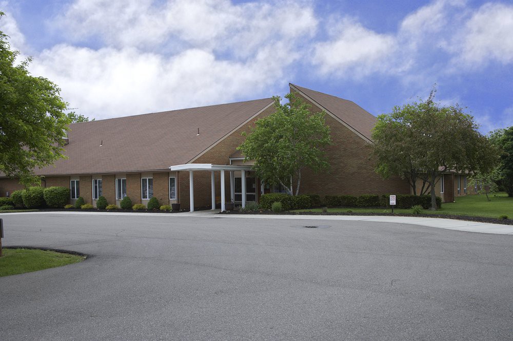 A church building with a sloped roof and a parking lot in the foreground.