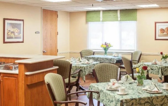 A cozy dining area with decorated tables and chairs, featuring a floral centerpiece and natural lighting.