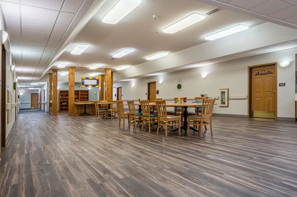 A spacious library interior with wooden tables and chairs, well-lit by overhead lights.