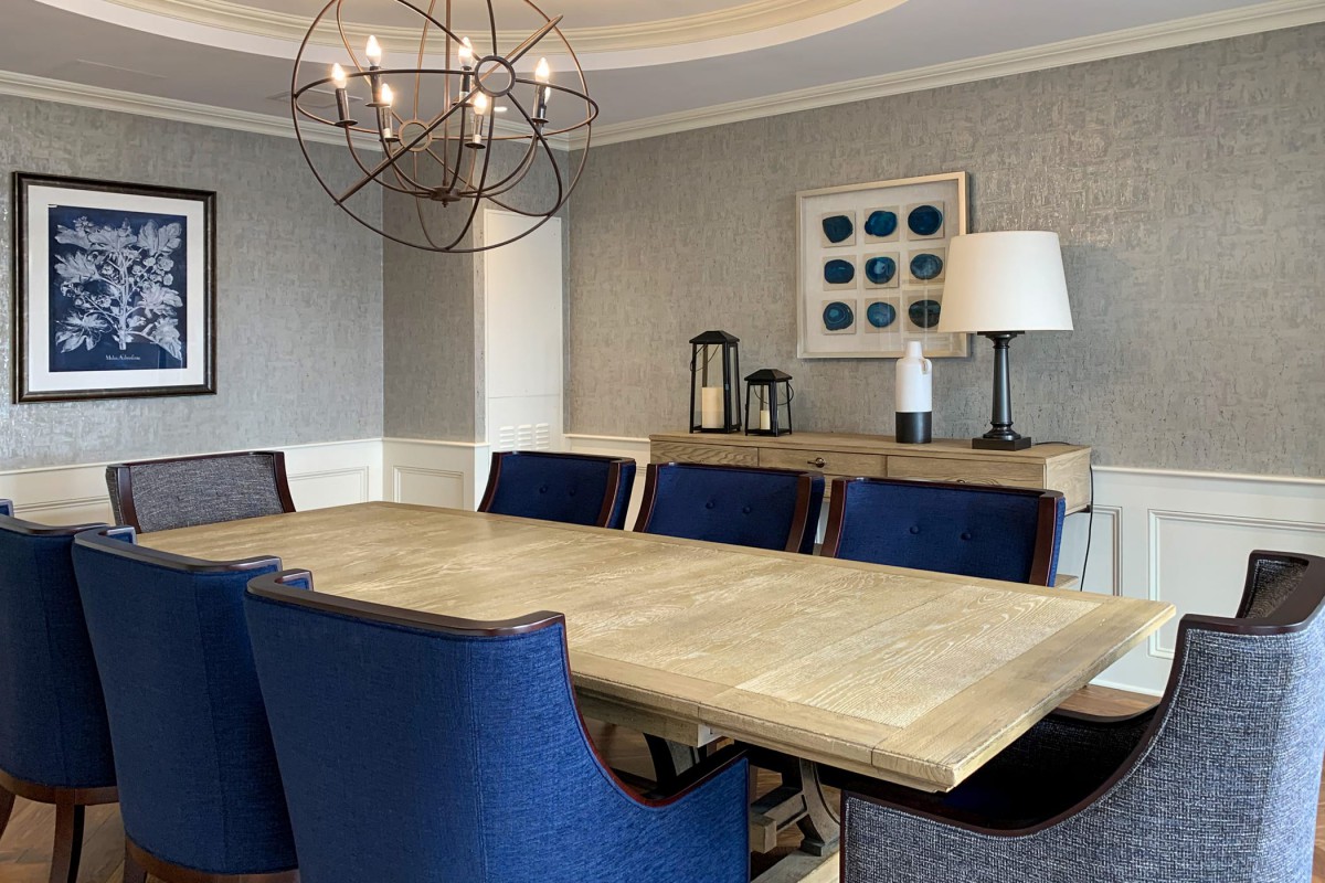 A modern dining room with a wooden table, blue upholstered chairs, and a stylish chandelier.