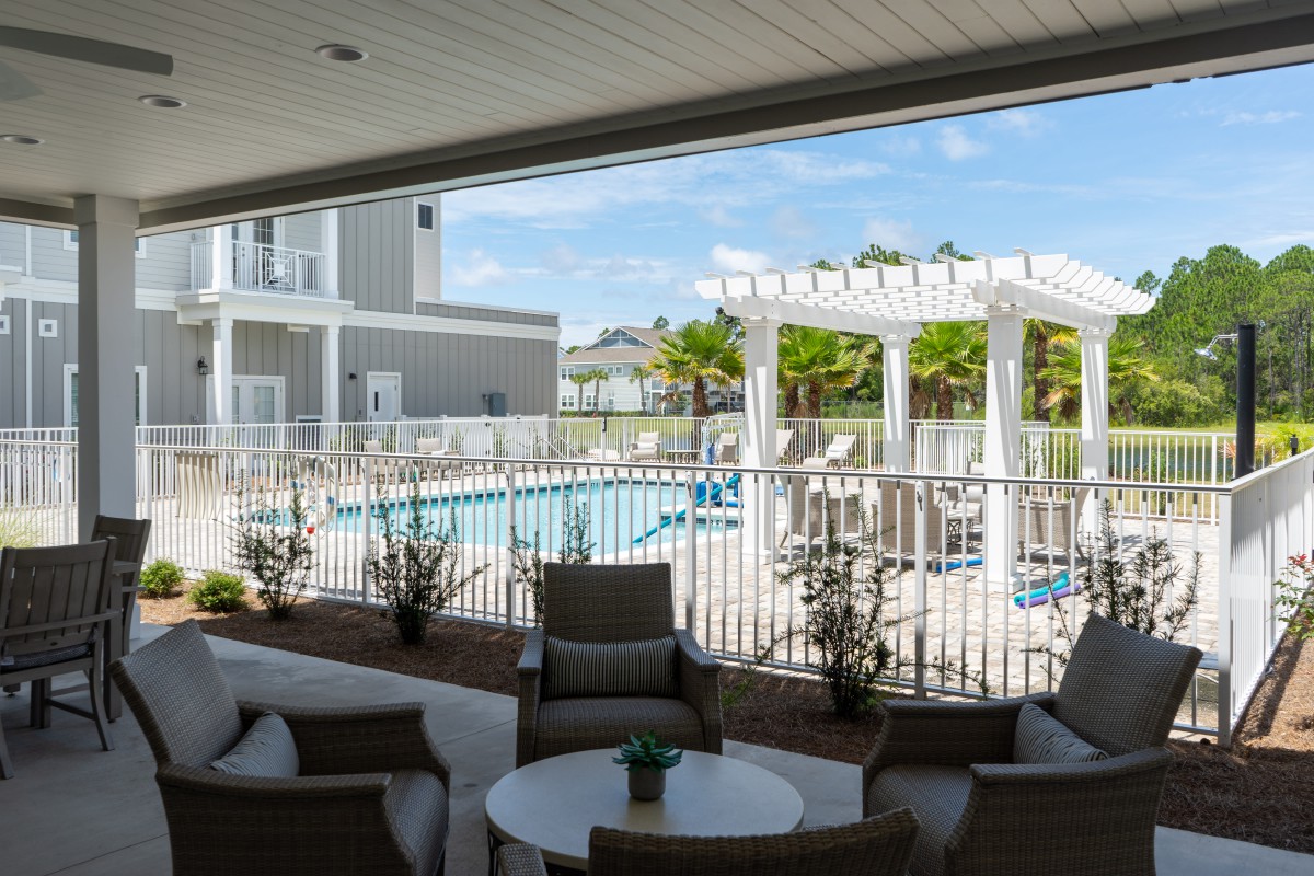 A view of a pool area with lounge chairs and a pergola, seen from an outdoor seating area.