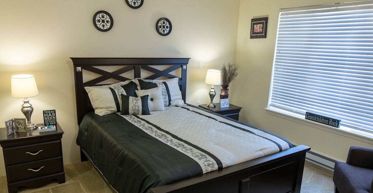A neatly arranged bedroom with a stylish bed, decorative pillows, and a bedside lamp.