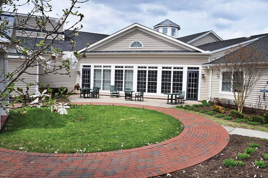 A beautifully designed house with a large window front and a curved brick pathway leading through a well-maintained lawn.