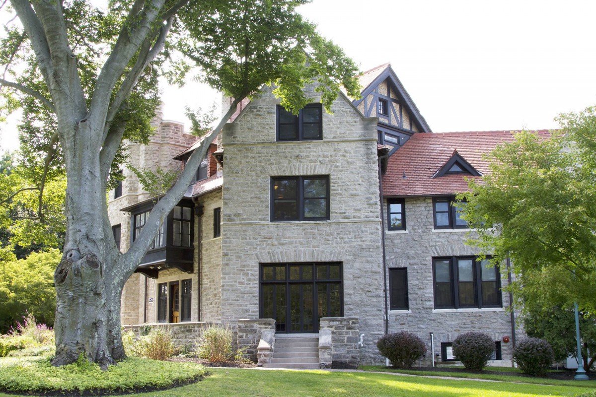 A large stone house with a red roof surrounded by greenery and trees.
