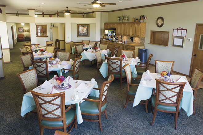 Bright dining room with neatly arranged tables and chairs, featuring a small kitchen area.