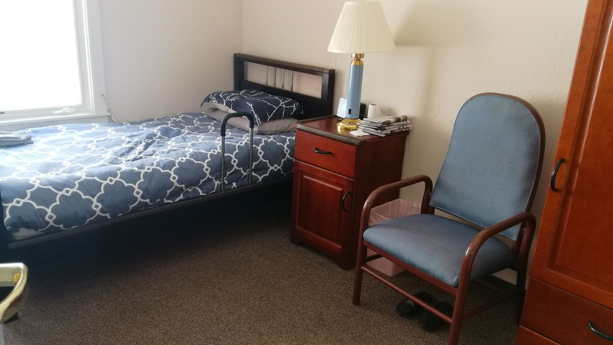 A simple bedroom with a single bed, nightstand, lamp, and chair.
