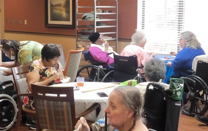 Elderly individuals in a nursing home dining area, some using wheelchairs.
