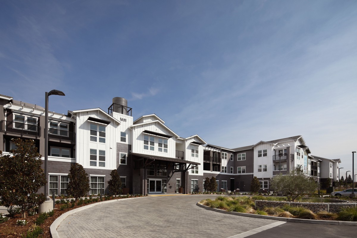 A modern residential apartment complex with landscaping and a clear blue sky.