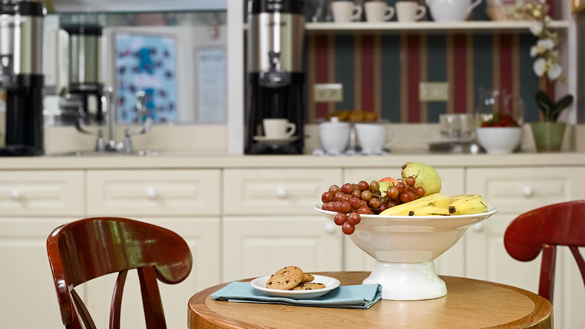 A cozy kitchen setup featuring a fruit bowl and cookies with a coffee machine in the background.