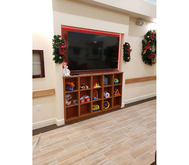 A TV mounted above shelves filled with toys, flanked by Christmas wreaths and decorations.