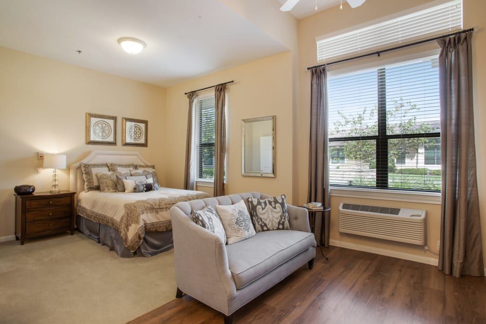 A cozy bedroom with a bed, small couch, and large window providing natural light.