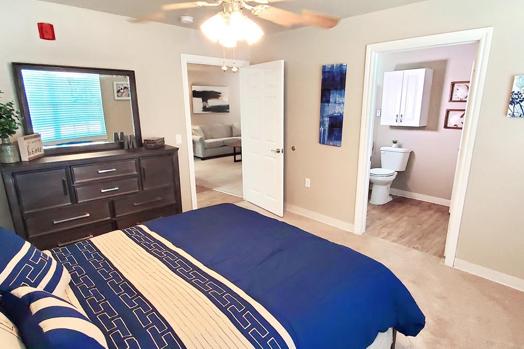 A cozy bedroom with a bed and dresser, leading to a bathroom.
