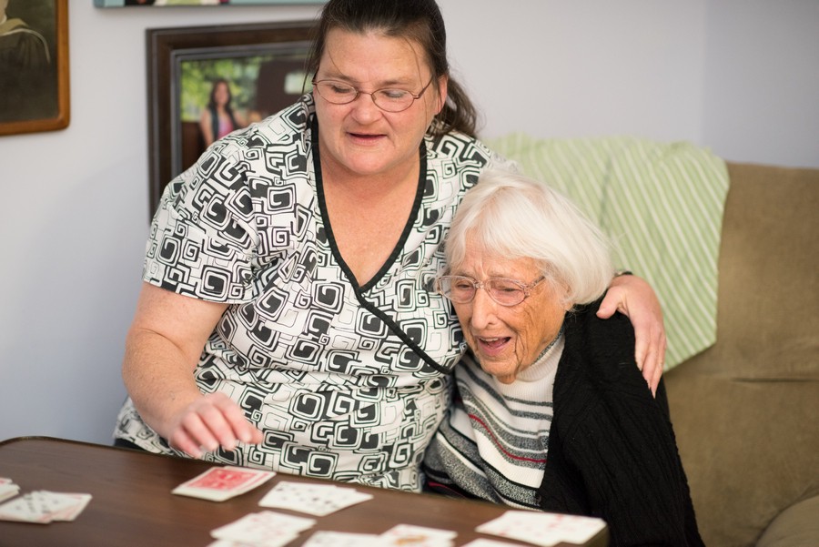 A caregiver and an elderly woman are enjoying a game of cards together, sharing smiles and companionship at a table indoors.