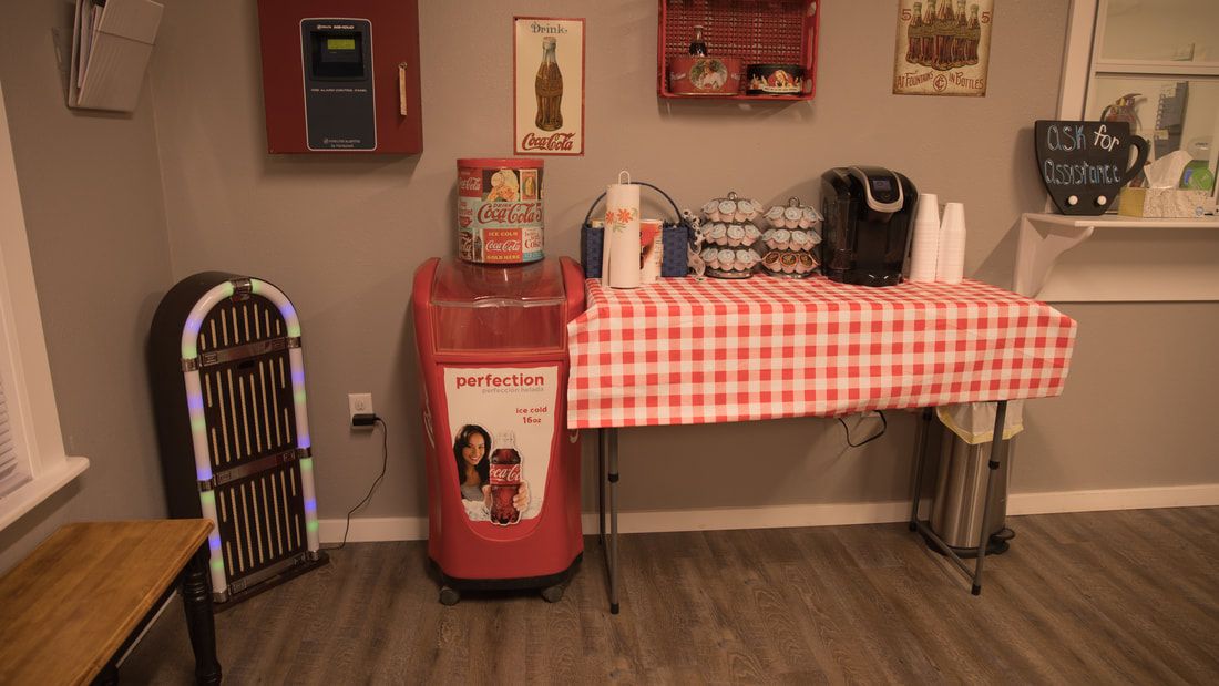 A cozy retro-themed corner featuring a red soda machine, checkered tablecloth, and vintage decor.