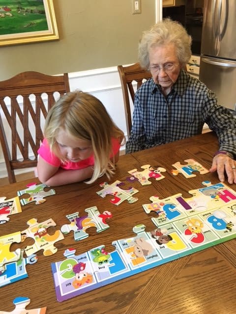 An elderly woman and a young girl working on a puzzle together at a table.