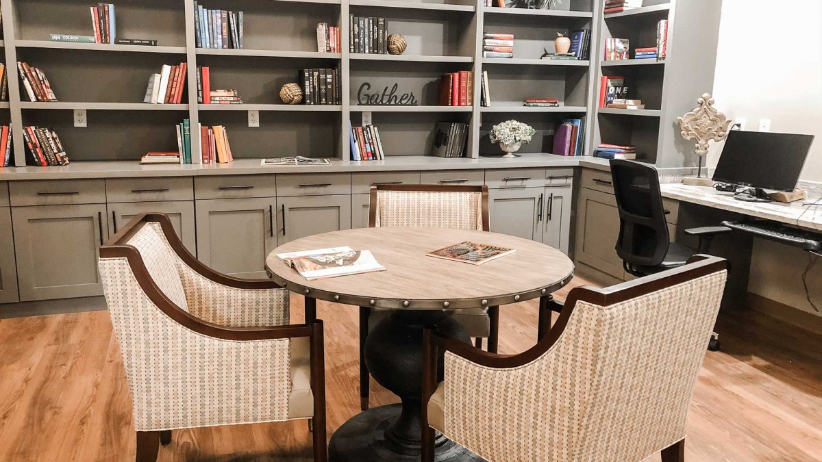 A cozy reading area featuring a round table surrounded by chairs, set against bookshelves filled with various items.