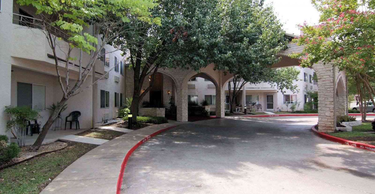 An arched entrance to a building with trees and a driveway.