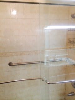 A tiled bathroom shower with a grab bar and glass door.