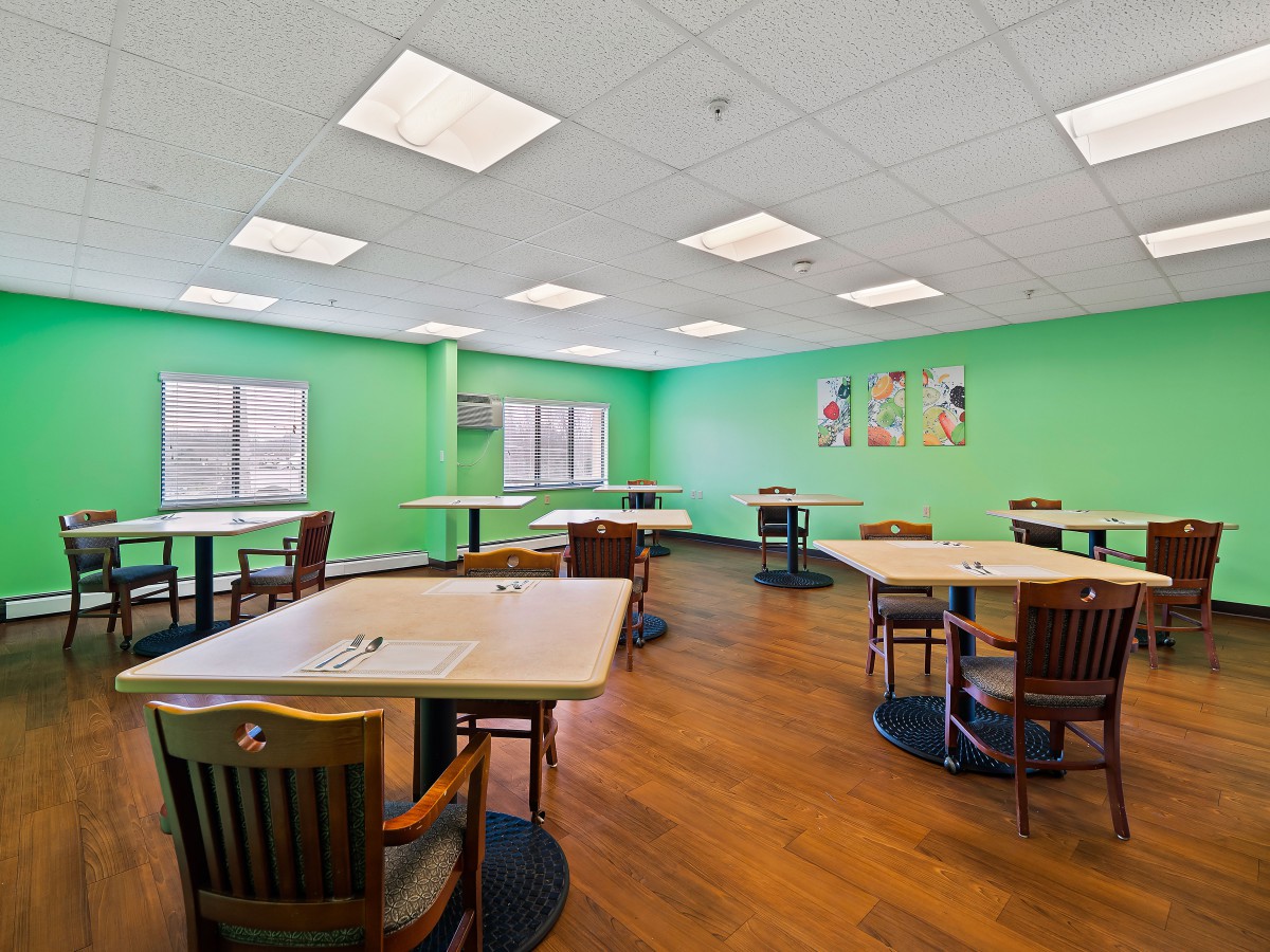 An empty dining room with green walls and neatly arranged tables and chairs.
