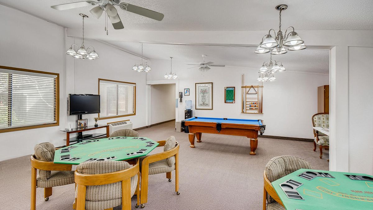 A spacious game room featuring a pool table and card tables, illuminated by ceiling lights and fans.