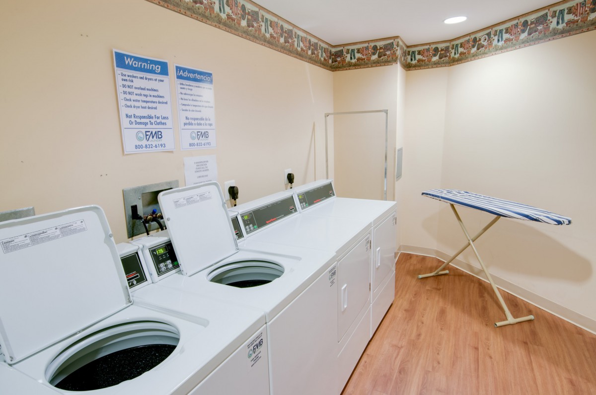 A well-organized laundry room featuring multiple washing machines and an ironing board.