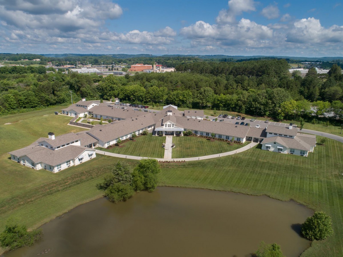 Aerial view of a campus with a central building surrounded by greenery and a pond.