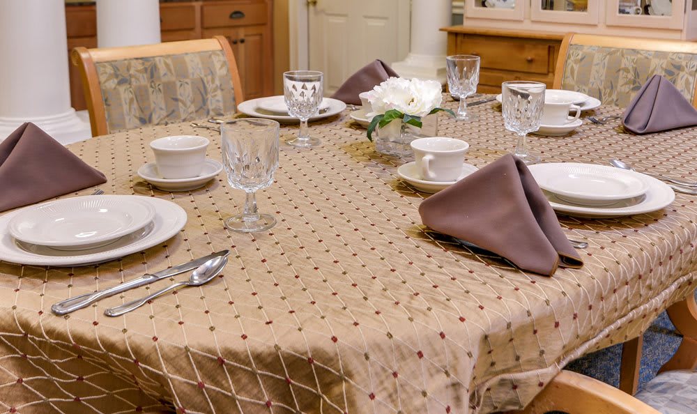 An elegantly set dining table with a patterned tablecloth, complete with dinnerware, glasses, and folded napkins.